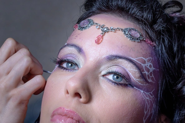 Gros plan sur une femme en cours de maquillage artistique avec des détails décoratifs autour des yeux
