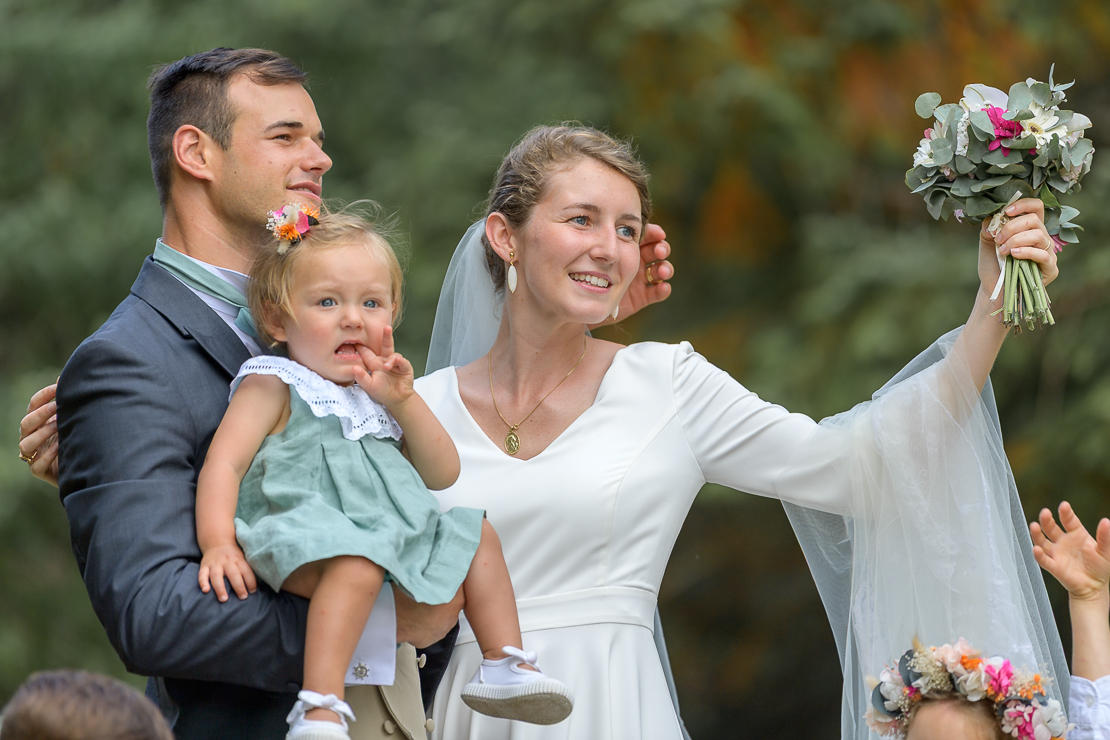 Mariée levant son bouquet tandis qu’un enfant est porté par le marié pendant un moment animé du mariage