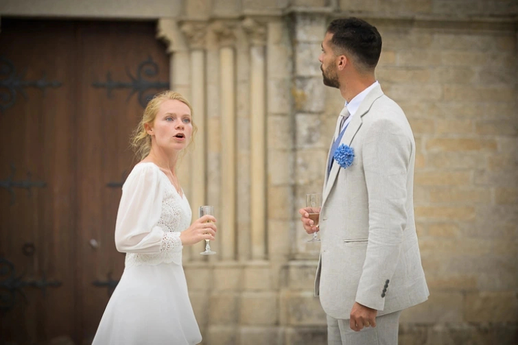 Couple de mariés discutant avec des verres à la main devant une église pendant leur mariage