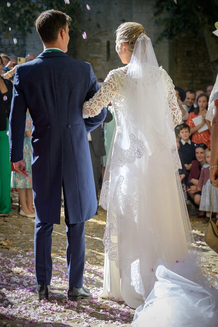 Les mariés vus de dos marchent parmi leurs invités lors de la sortie de cérémonie, sous des pétales au sol