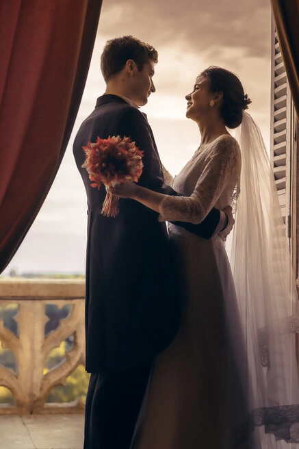 Couple de mariés enlacés face à face près d’une fenêtre, éclairés par une lumière naturelle douce