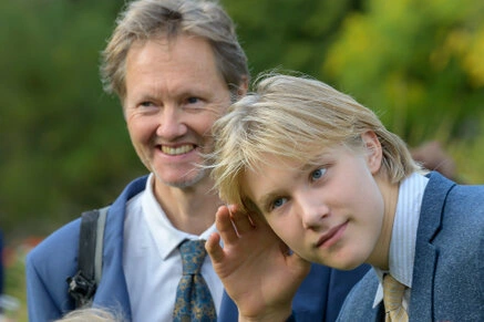 Un homme et un enfant souriants et complices pendant un mariage en extérieur