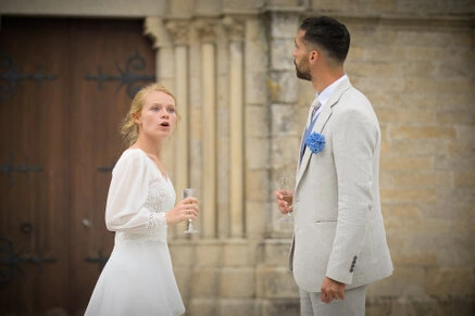 Couple de mariés discutant avec des verres à la main devant une église pendant leur mariage