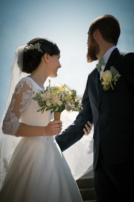 Les mariés marchent ensemble en extérieur, la mariée tenant son bouquet dans une lumière naturelle