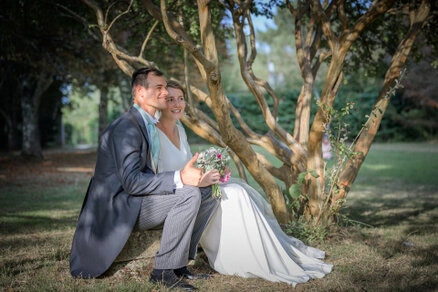 Couple de mariés assis ensemble sous un arbre dans un jardin, moment calme lors d’un mariage