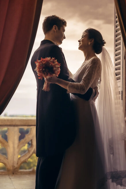 Couple de mariés enlacés face à face près d’une fenêtre, éclairés par une lumière naturelle douce