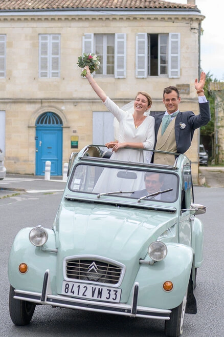 Couple de mariés debout dans une voiture ancienne décapotable saluant les invités pendant leur mariage