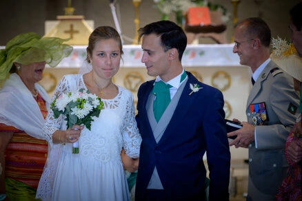 Les mariés entourés de leurs proches à la sortie de la cérémonie, tenant un bouquet de fleurs