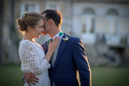 Marié embrassant la mariée sur le front, moment tendre en extérieur lors d’un mariage
