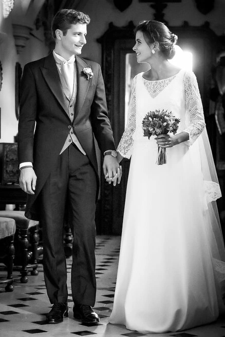 Couple de mariés se tenant la main et se regardant avec complicité dans un intérieur, en noir et blanc