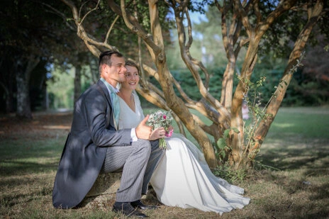 Couple de mariés assis ensemble sous un arbre dans un jardin, moment calme lors d’un mariage