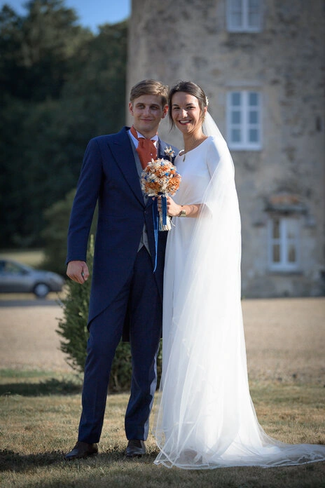 Couple de mariés posant ensemble devant un bâtiment en pierre lors d’un mariage en extérieur