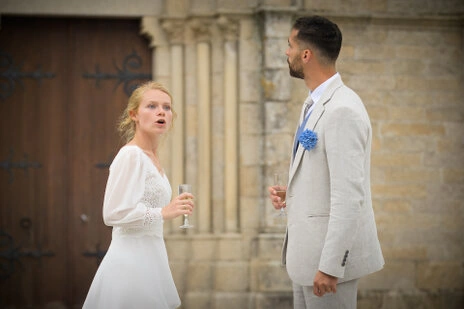 Couple de mariés discutant avec des verres à la main devant une église pendant leur mariage