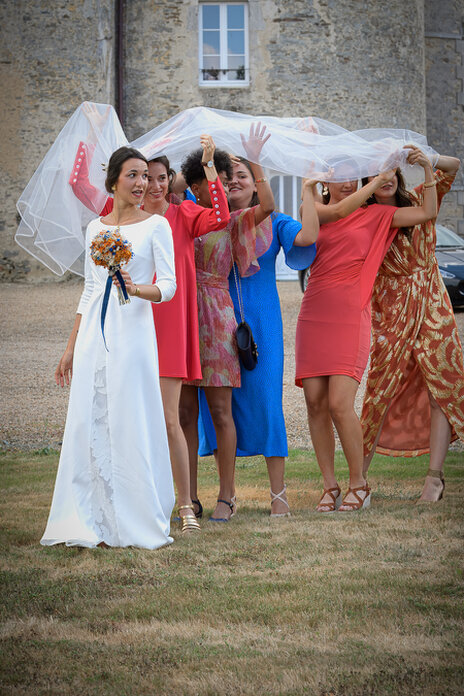 Mariée accompagnée de ses amies sous son voile, moment spontané et joyeux lors d’un mariage