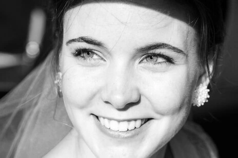 Gros plan sur le visage de la mariée souriante en noir et blanc, regardant vers l’objectif