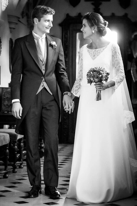 Couple de mariés se tenant la main et se regardant avec complicité dans un intérieur, en noir et blanc