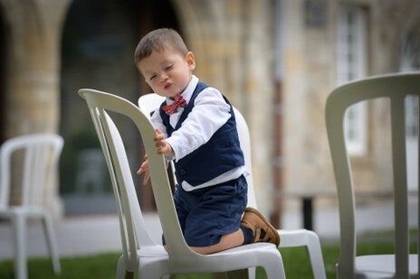 Jeune enfant en tenue élégante jouant sur une chaise pendant le vin d’honneur d’un mariage
