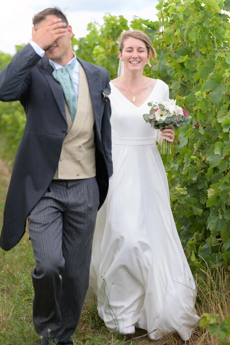 Couple de mariés marchant dans un vignoble, moment naturel et spontané lors d’un mariage