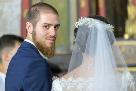 Le marié se retourne et regarde vers l’objectif pendant la cérémonie, aux côtés de la mariée voilée