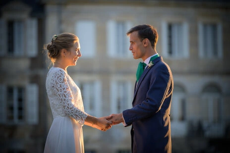Couple de mariés se tenant les mains face à face en extérieur, éclairés par une lumière douce de fin de journée