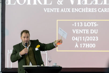 Homme prenant la parole avec un micro et levant une pancarte lors d’une vente aux enchères en entreprise