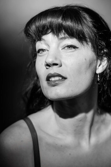 Portrait en noir et blanc d’une femme avec éclairage contrasté, regard légèrement hors cadre et expression affirmée