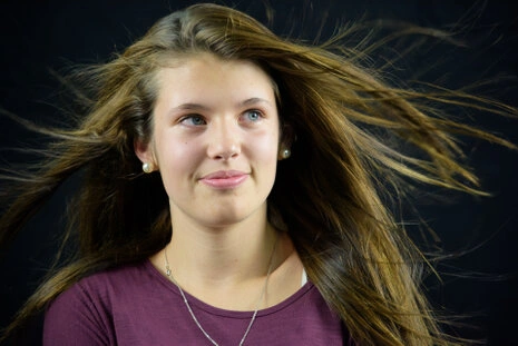 Portrait d’une femme en studio avec cheveux en mouvement, regard détourné et expression naturelle sur fond sombre