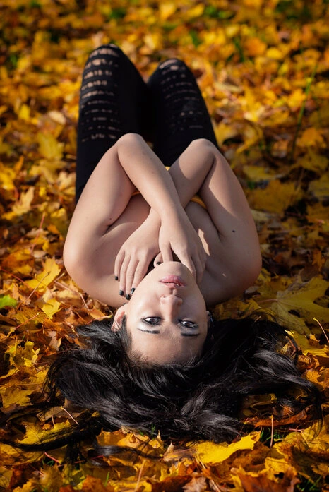 Portrait d’une femme allongée sur un sol recouvert de feuilles d’automne, regard dirigé vers l’objectif, composition graphique