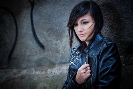 Portrait d’une femme en extérieur contre un mur en pierre, portant une veste en cuir, éclairée au flash avec un rendu naturel