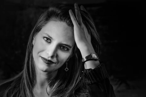 Portrait en noir et blanc d’une femme avec un léger sourire, regard direct et main dans les cheveux, ambiance élégante