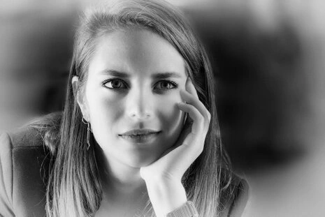 Portrait en noir et blanc d’une femme regardant l’objectif, main posée sur le visage, arrière-plan flou