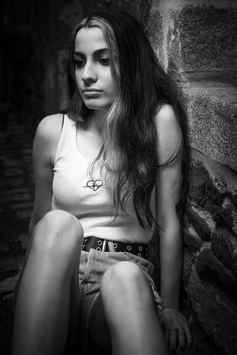 Portrait en noir et blanc d’une femme assise contre un mur, expression introspective et lumière contrastée