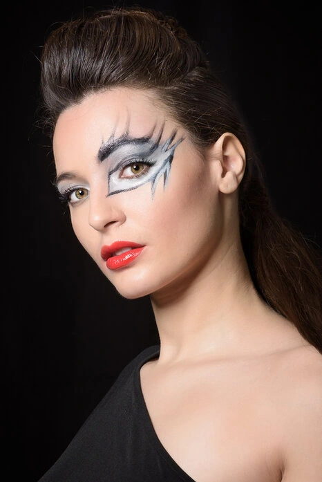 Portrait d’une femme avec maquillage graphique et regard intense, éclairage précis sur fond sombre mettant en valeur les traits du visage