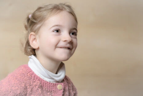 Portrait d’une enfant avec une expression douce et souriante, éclairée par une lumière naturelle délicate sur fond neutre