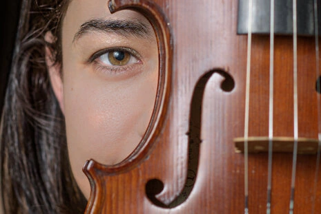 Portrait rapproché d’une femme partiellement cachée derrière un violon, mettant en valeur un regard et les détails de l’instrument