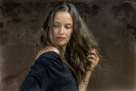 Portrait d’une femme avec regard détourné, cheveux en mouvement et expression douce dans une lumière naturelle