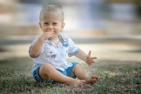 Portrait d’un jeune enfant assis dans l’herbe, en train de jouer avec naturel et spontanéité, expression joyeuse