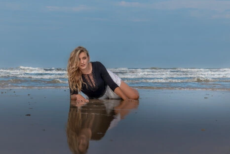 Portrait d’une femme allongée sur le sable en bord de mer, avec un reflet dans l’eau et une lumière naturelle