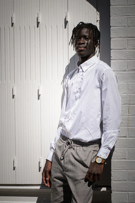 Portrait d’un homme en extérieur, adossé à un mur, avec une lumière directe créant des contrastes marqués