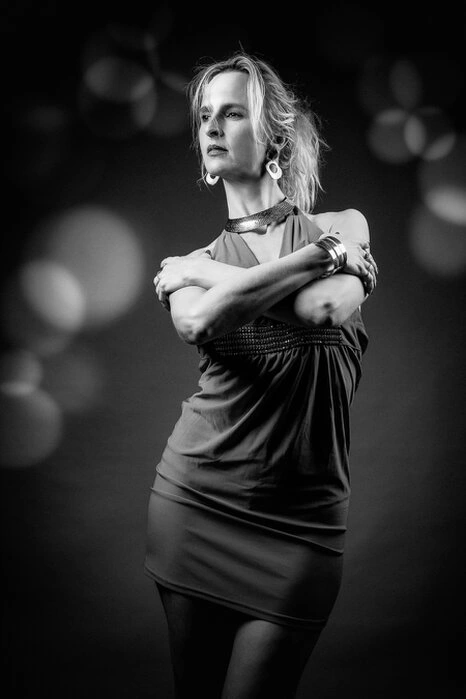 Portrait d’une femme en noir et blanc, debout avec une posture affirmée et une lumière contrastée mettant en valeur la silhouette