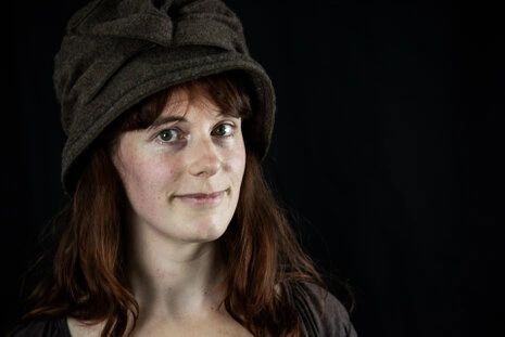 Portrait d’une femme en studio portant un chapeau, regard naturel et expression douce sur fond sombre