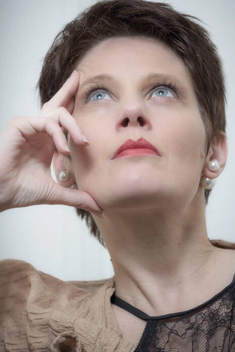 Portrait d’une femme en studio regardant vers le haut, main posée sur le visage, expression calme et réfléchie