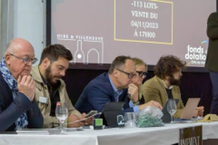 Groupe de professionnels assis à une table utilisant ordinateurs et téléphones lors d’une vente aux enchères ou événement professionnel