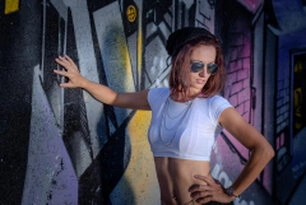 Portrait d’une femme en extérieur devant un mur graffiti, pose dynamique avec lunettes de soleil et éclairage au flash