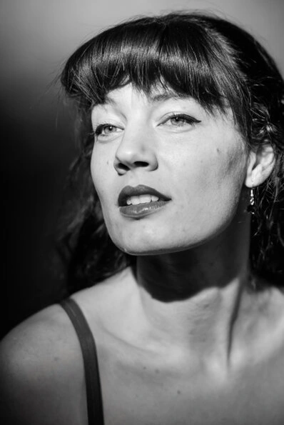 Portrait en noir et blanc d’une femme avec éclairage contrasté, regard légèrement hors cadre et expression affirmée
