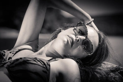 Portrait en noir et blanc d’une femme allongée en extérieur, portant des lunettes de soleil, pose détendue et lumière contrastée