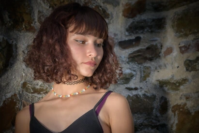 Portrait d’une femme en extérieur contre un mur en pierre, regard détourné et expression naturelle avec une lumière douce